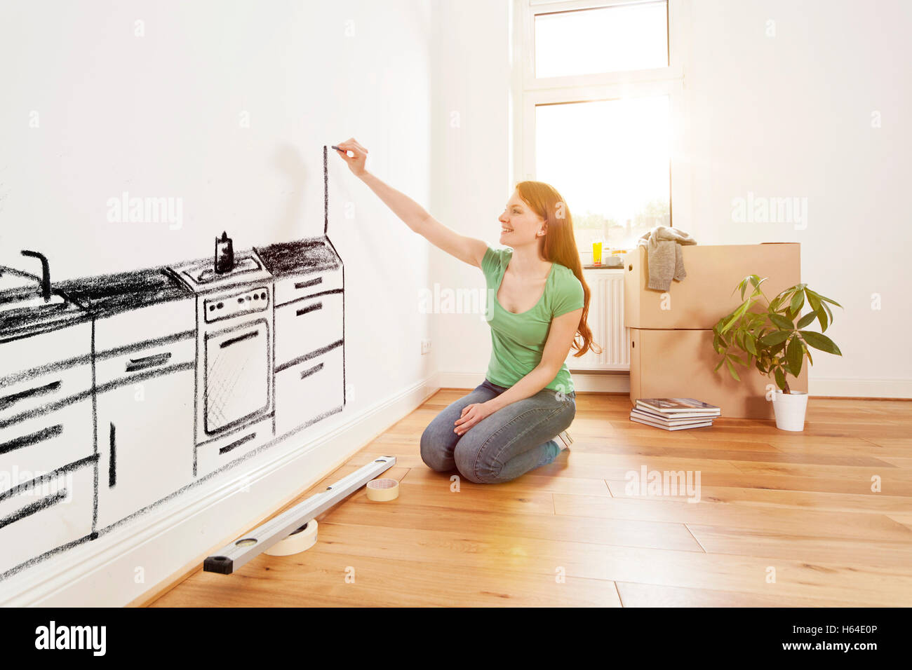 Young woman drawing a kitchen on a wall in new apartment Stock Photo