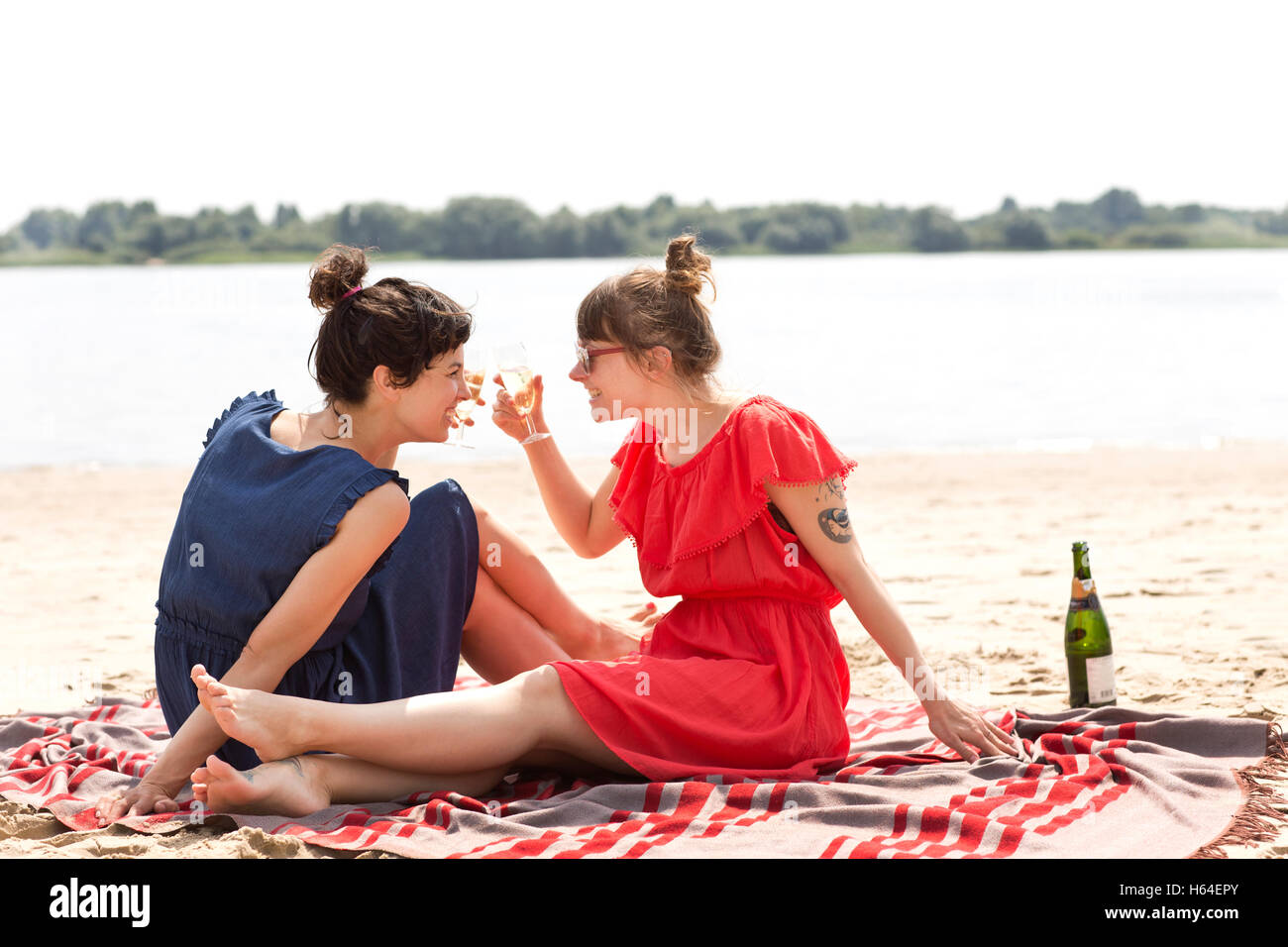 Two smiling friends sitting on the beach toasting with glasses of