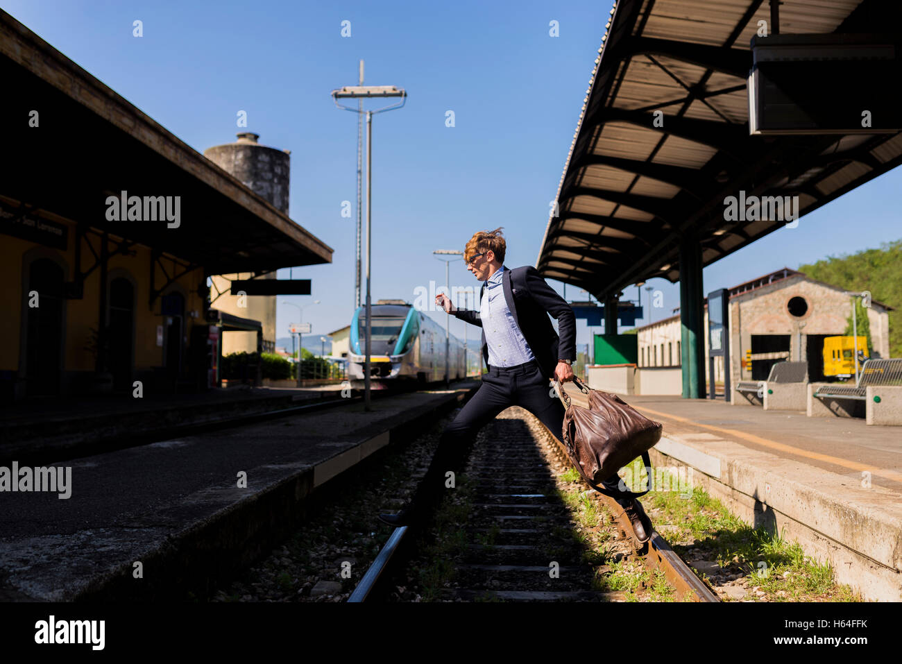 Young businessman jumping over tracks at train station Stock Photo Alamy