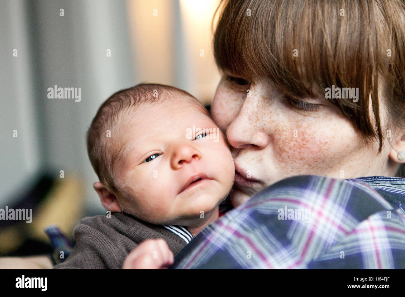 Freckled mother kissing her newborn baby son on the cheek Stock Photo