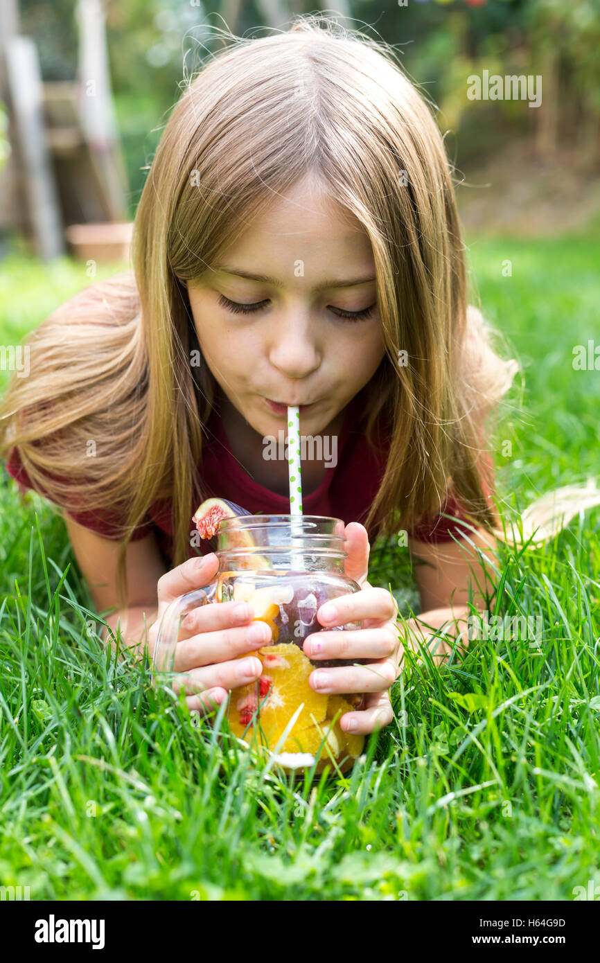 Girl lying on a meadow drinking infused water with various fruits Stock