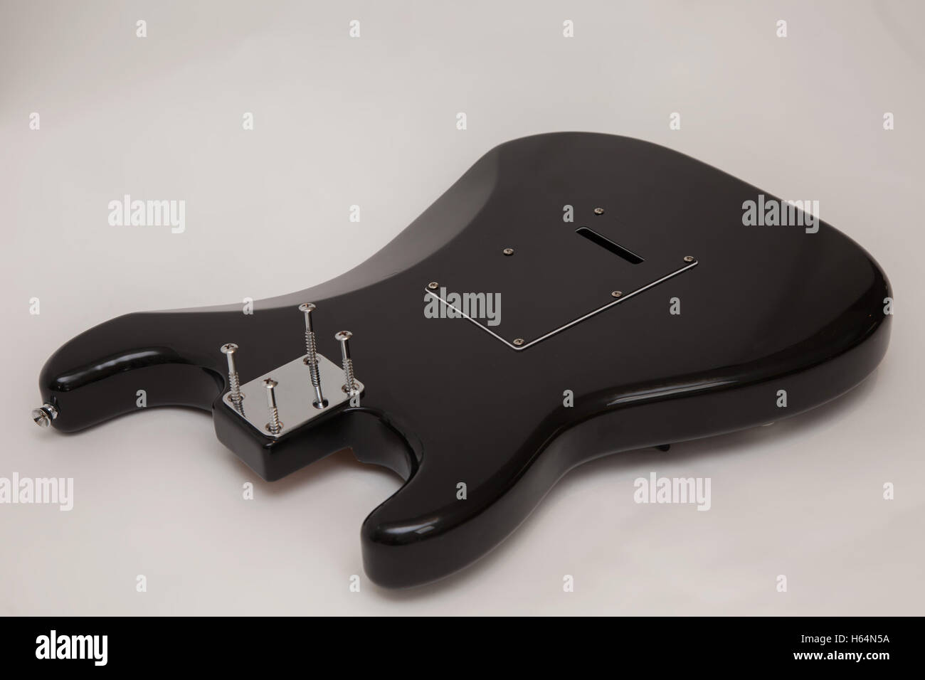 Back of a black fender stratocaster copy electric guitar body, neck removed, with the screws loosened Stock Photo