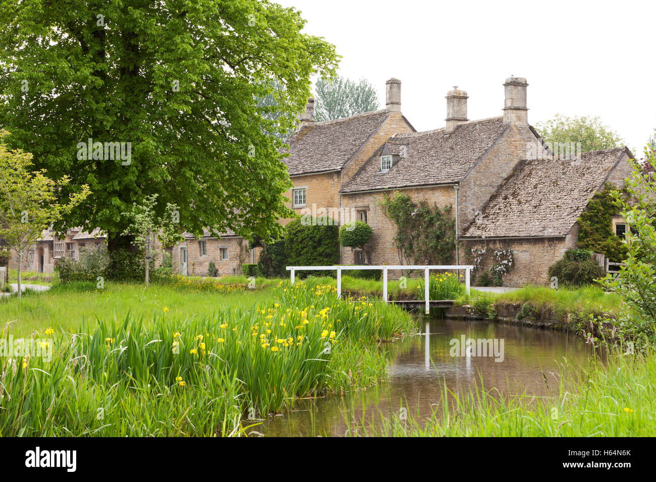 Row of stone houses near wooden bridge over small river in rural English village on overcast day Stock Photo