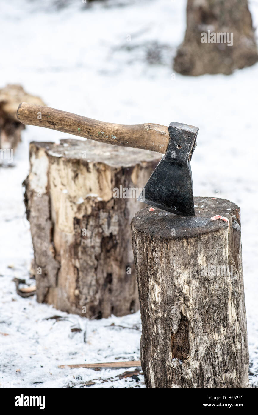 Ax stuck in log of wood on the background of the winter forest and huts. Stock Photo