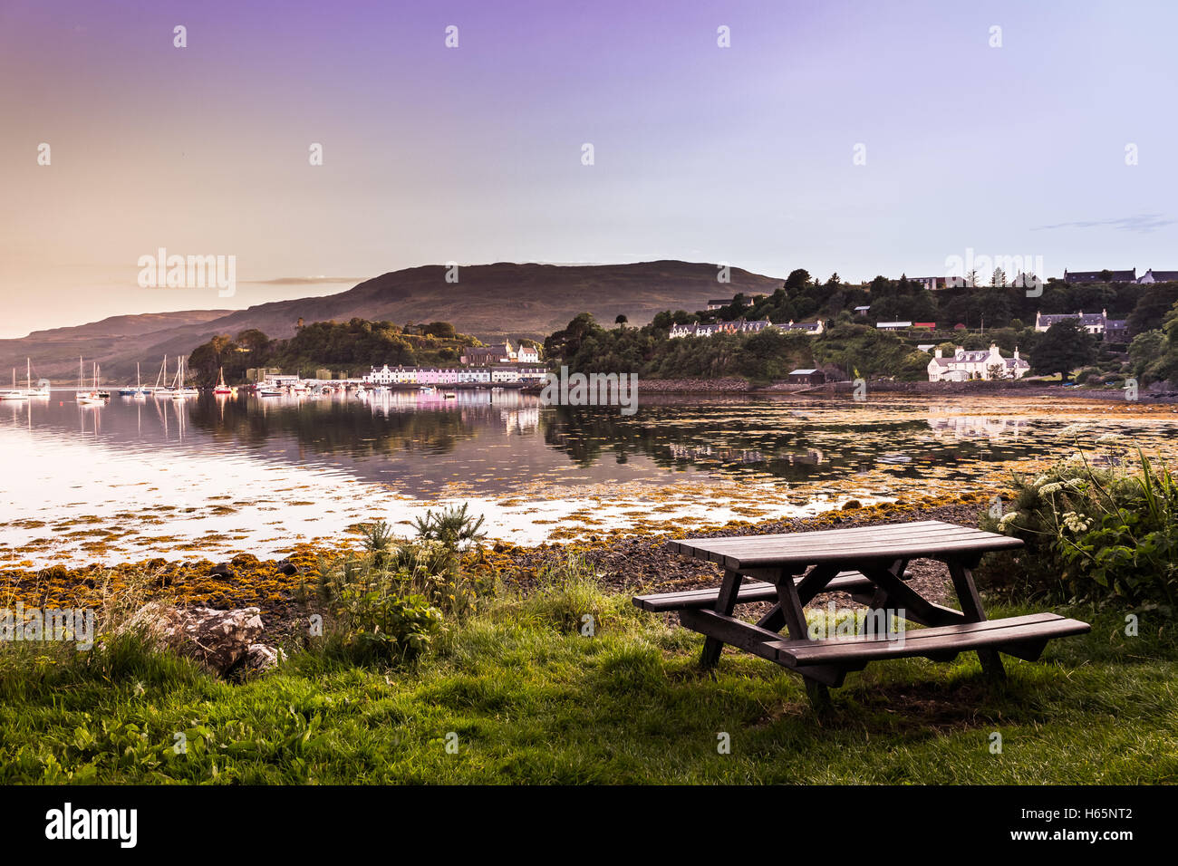 Empty Picnic Table At A Bay During Sunset With View Of Colorful Houses And Sail Boats In The Distance Stock Photo