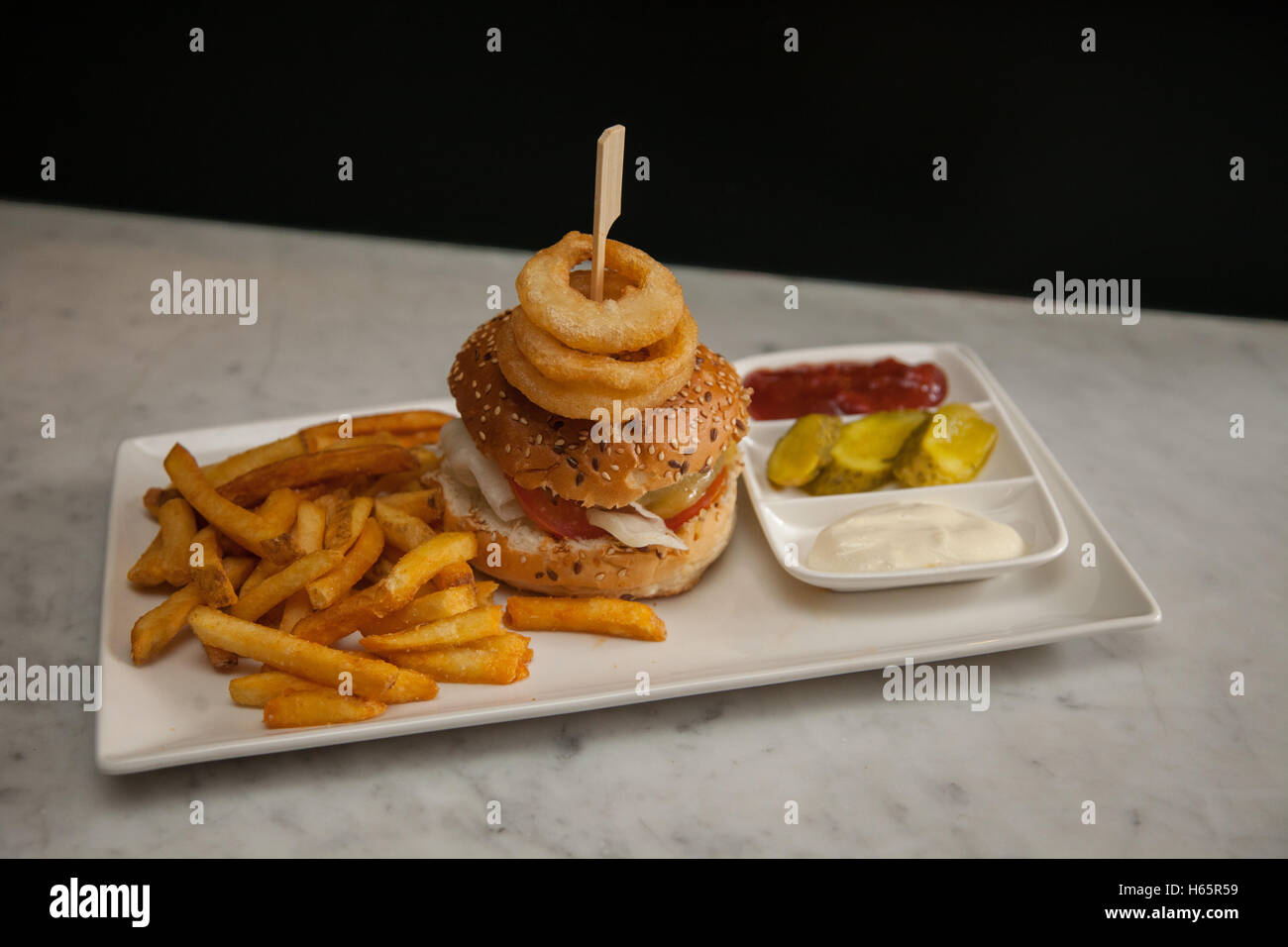 A cheeseburger, french fries, onion rings, ketchup, mayonnaise on an oblong white plate Stock Photo
