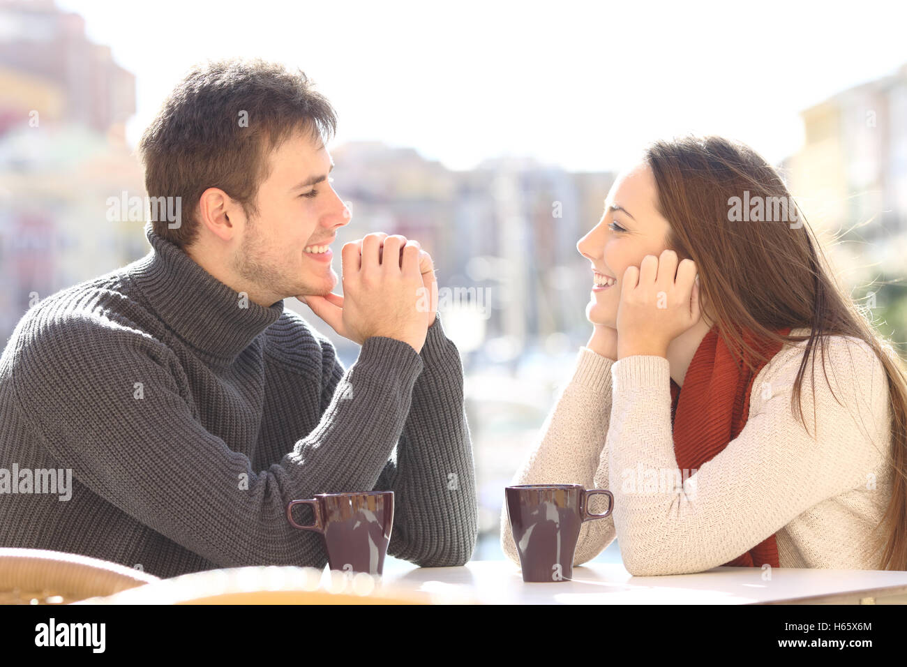 Side view of a happy couple dating and flirting in love looking each other in a bar terrace with a port of urbanization Stock Photo