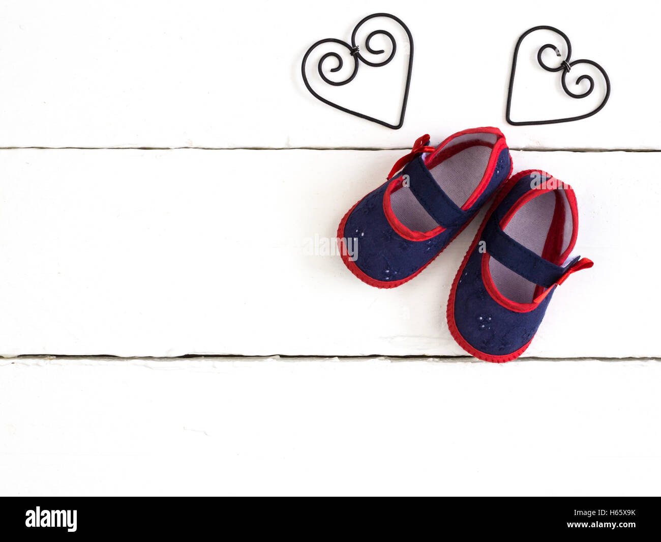 Overhead photo of pair of navy and red baby booties, heart metal frame shapes isolated on white wood table Stock Photo