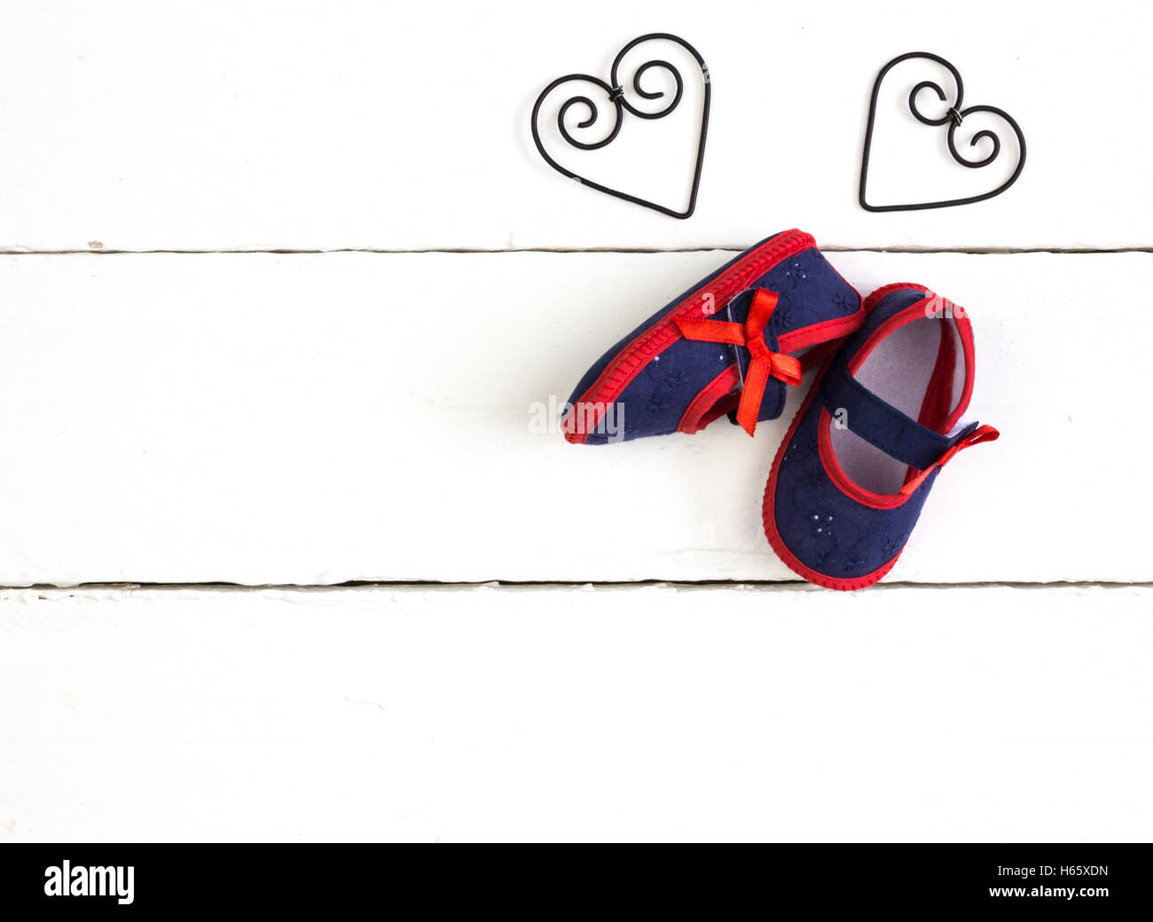 Overhead photo of pair of navy and red baby booties, heart metal frame shapes isolated on painted white wood table Stock Photo