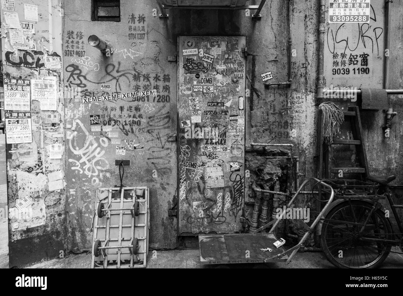Graffiti, stickers and posters on a dirty and aged wall at some shady back street in Tsim Sha Tsui, Kowloon, Hong Kong, China. Stock Photo