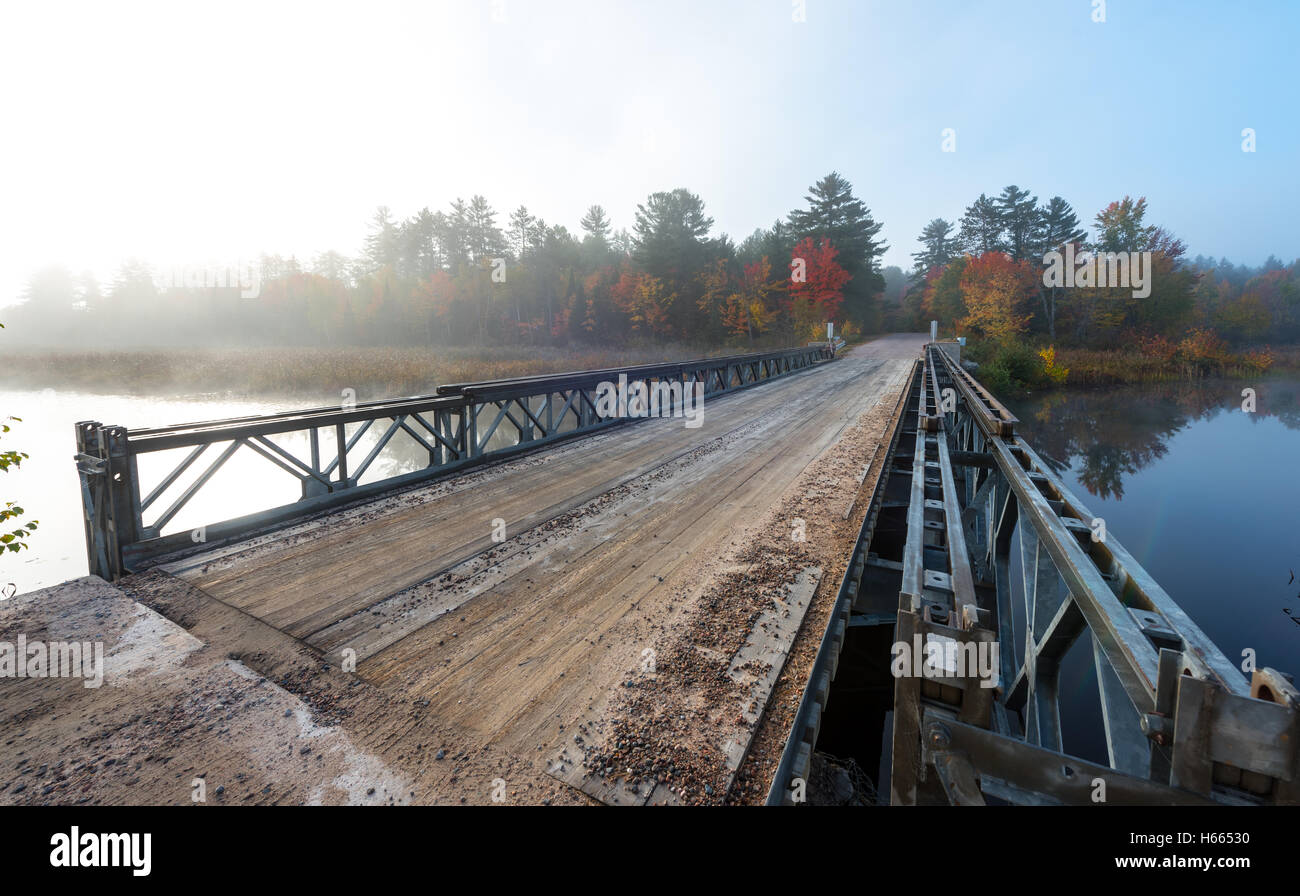 October morning sun shines on a single lane steel and timber bridge over Corry Lake. Stock Photo