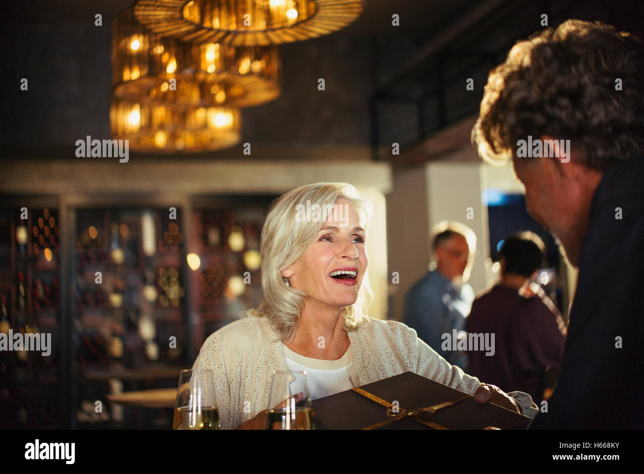 Senior woman receiving gift from husband at bar Stock Photo