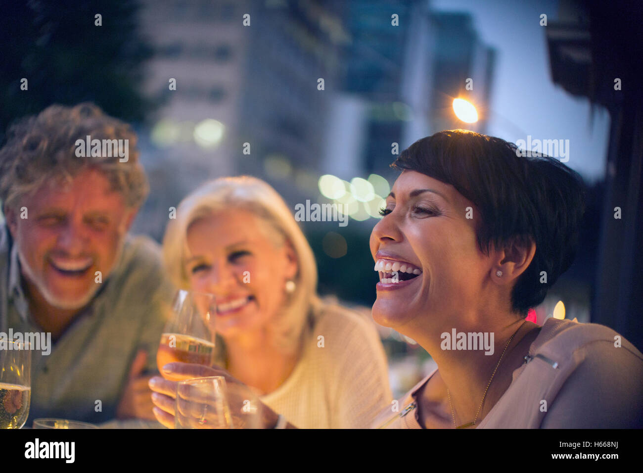 Laughing friends drinking white wine at urban sidewalk cafe Stock Photo
