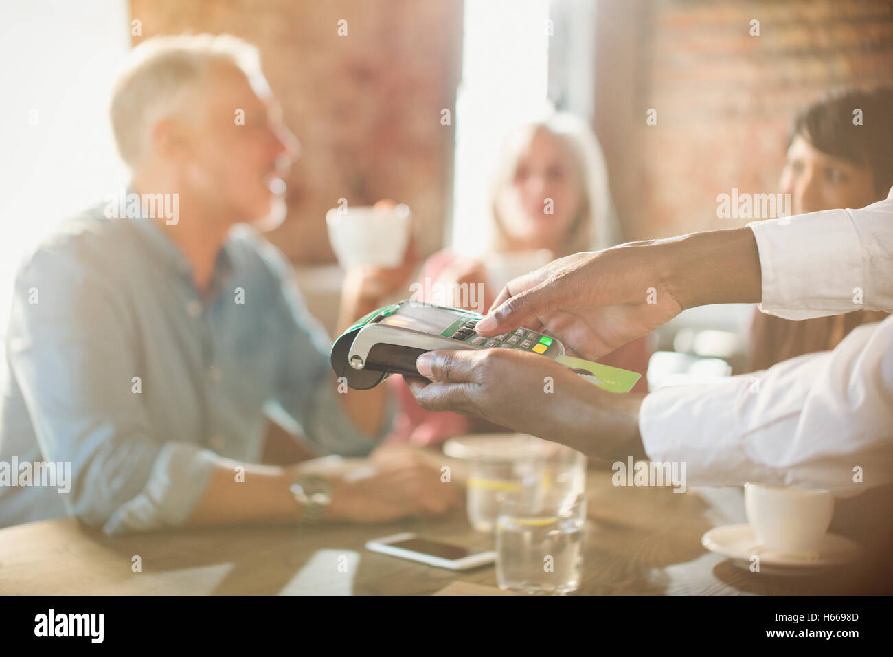 Waiter using credit card reader at restaurant table Stock Photo