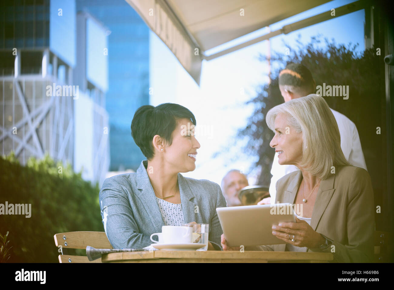 Businesswomen using digital tablet at urban sidewalk cafe Stock Photo ...
