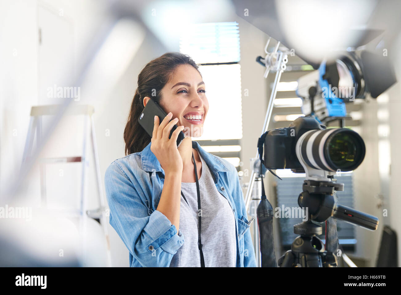 Smiling female photographer talking on cell phone behind camera in studio Stock Photo