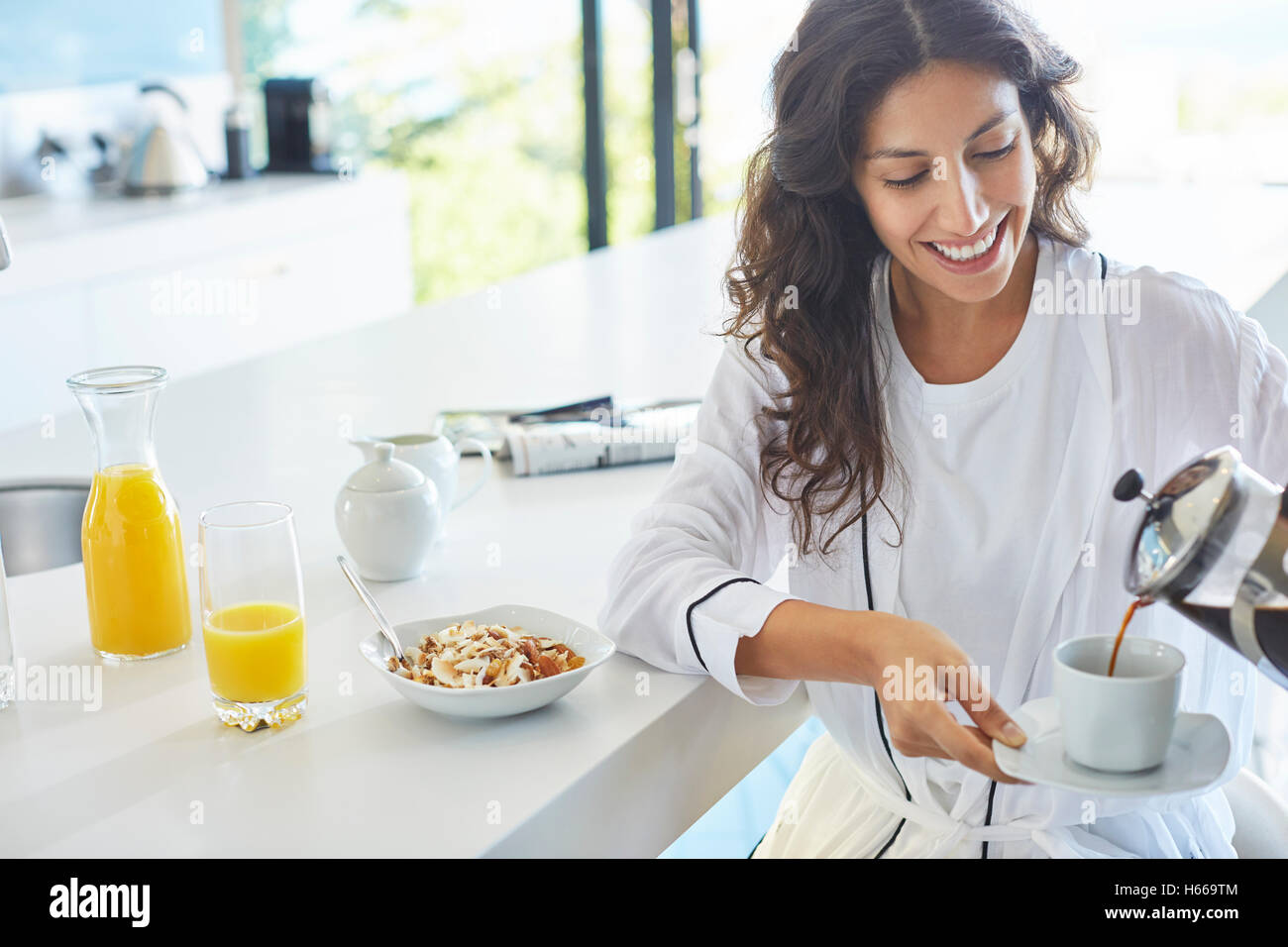 Smiling woman in bathrobe pouring French press coffee in kitchen Stock Photo