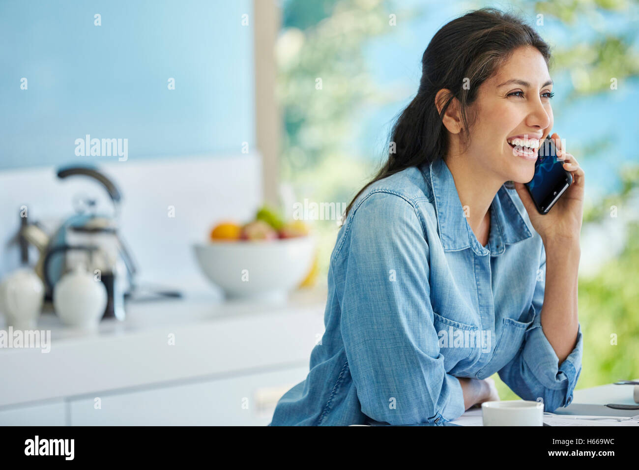 Smiling woman talking on cell phone in kitchen Stock Photo