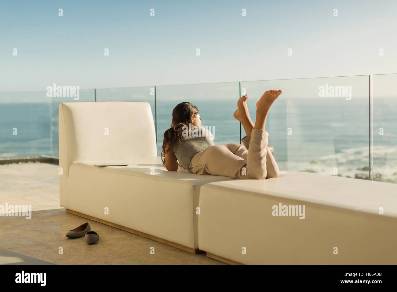 Woman on luxury balcony relaxing laying on bench looking at sunny ocean view Stock Photo