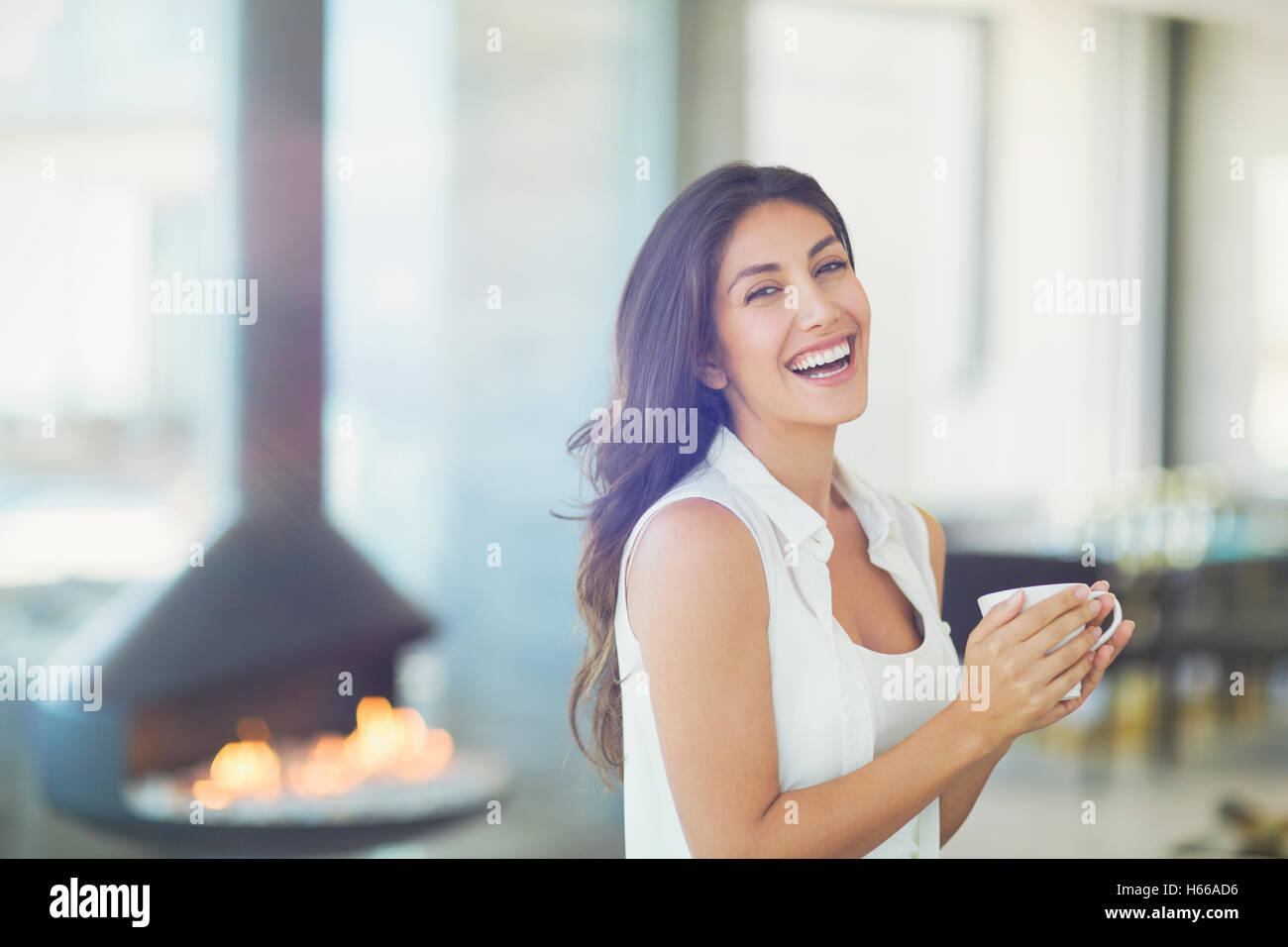 Portrait smiling woman drinking coffee near fireplace Stock Photo