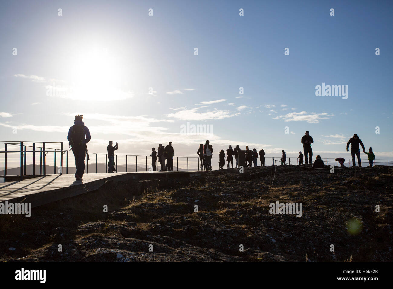 Toursits visting the rift valley in the Pingvellir national Park home of the ancient Icelandic parliement in Iceland, walk silhouetted against thje sun on top of the cliff. Stock Photo