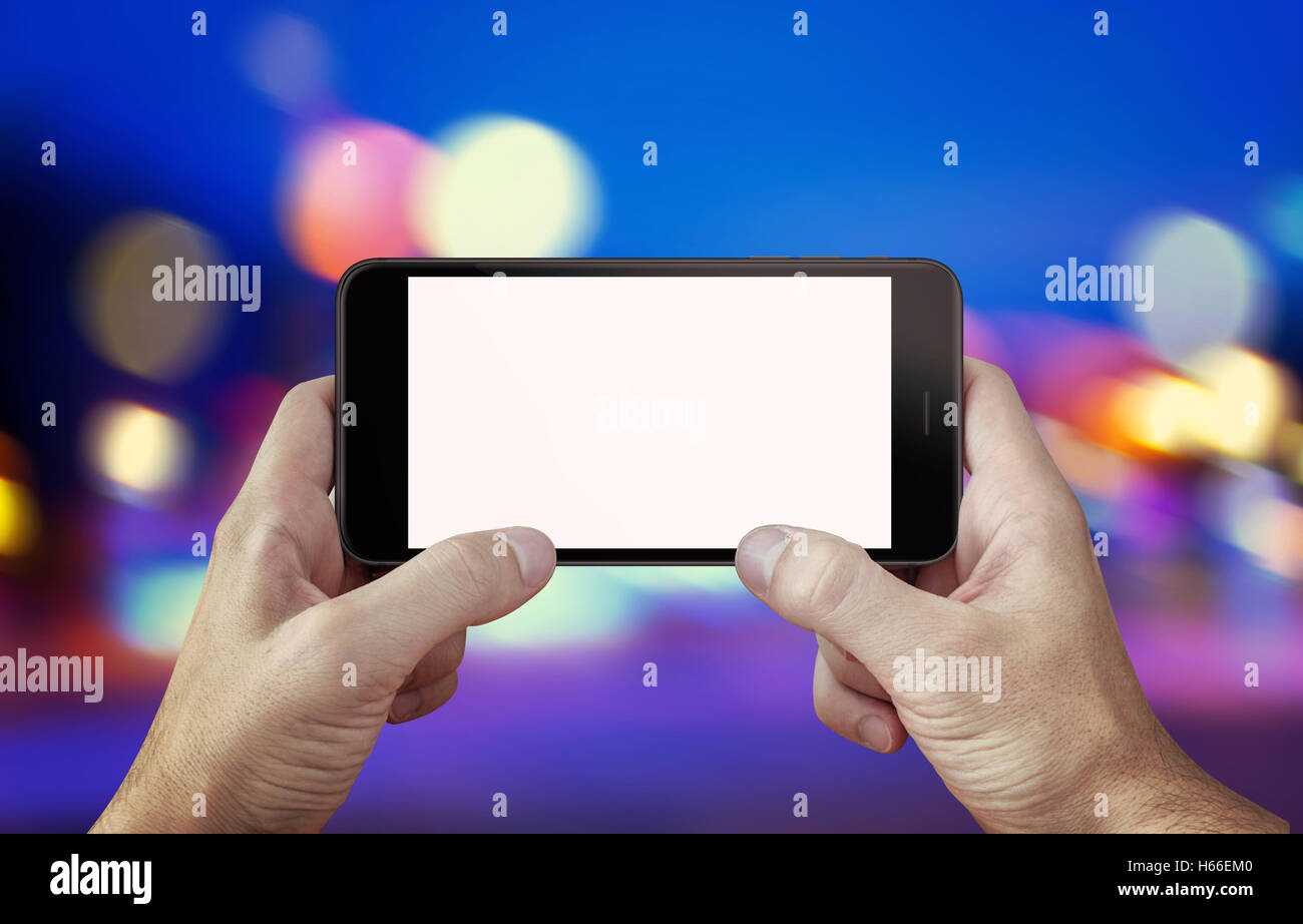 Use camera or play game on mobile phone with isolated display mockup. Phone in hands, horizontal position. City, night lights in Stock Photo