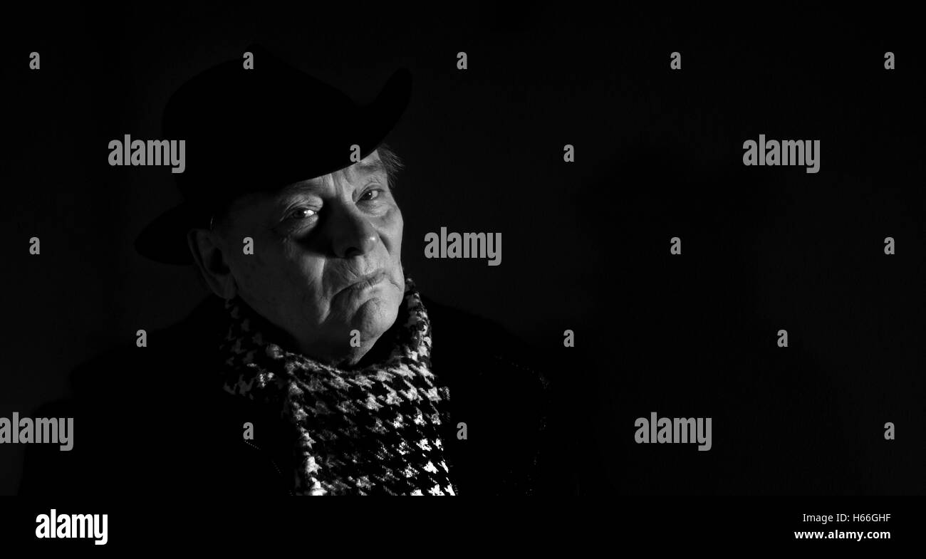 Portrait of elderly man in coat, hat and scarf on a dark background Stock Photo