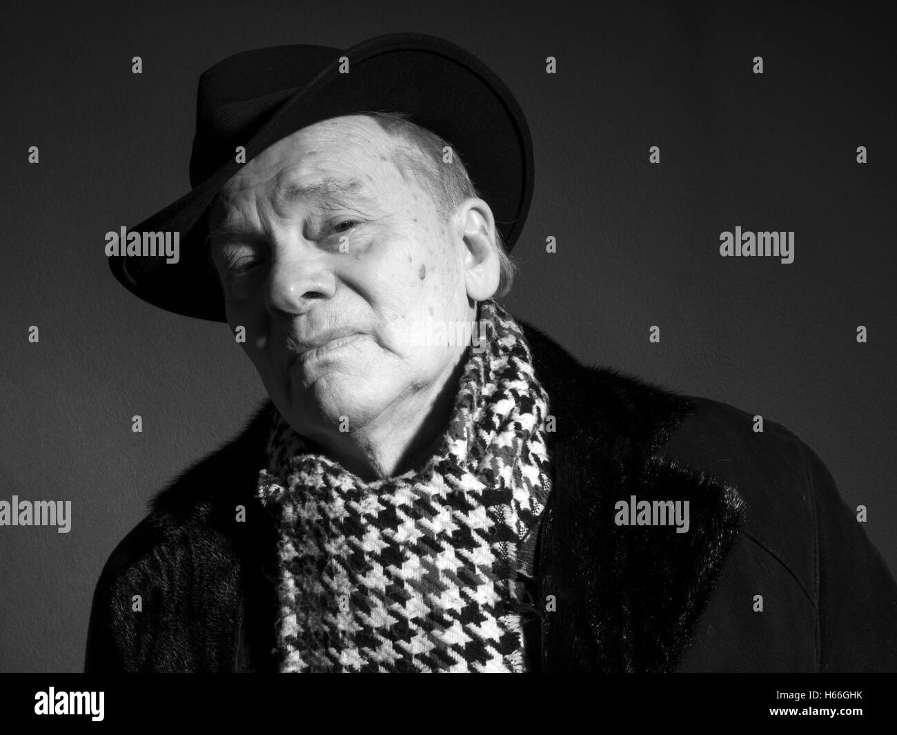 Portrait of elderly man in coat, hat and scarf on a dark background Stock Photo