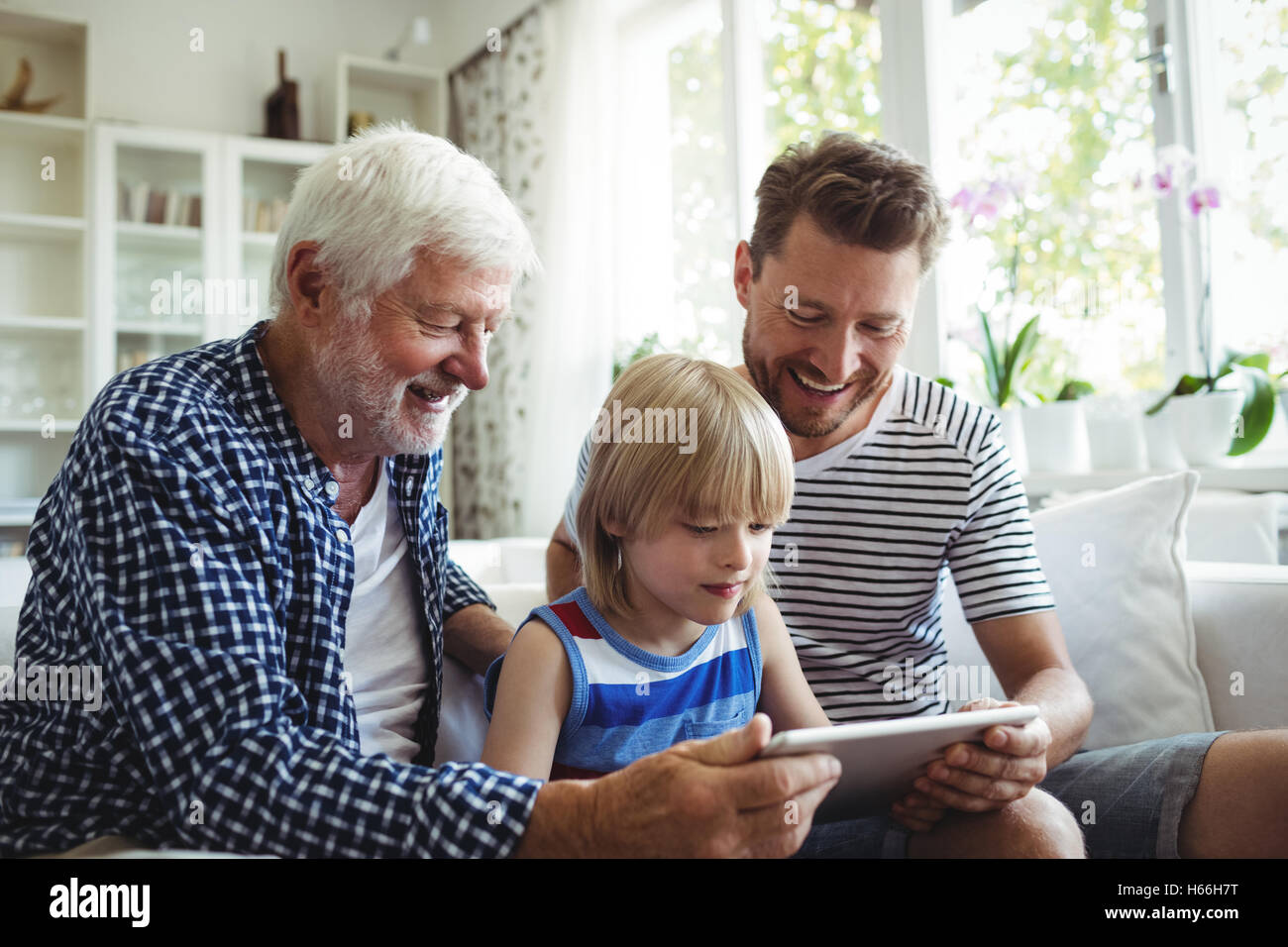 Boy using digital tablet with his father and grandfather in living room Stock Photo