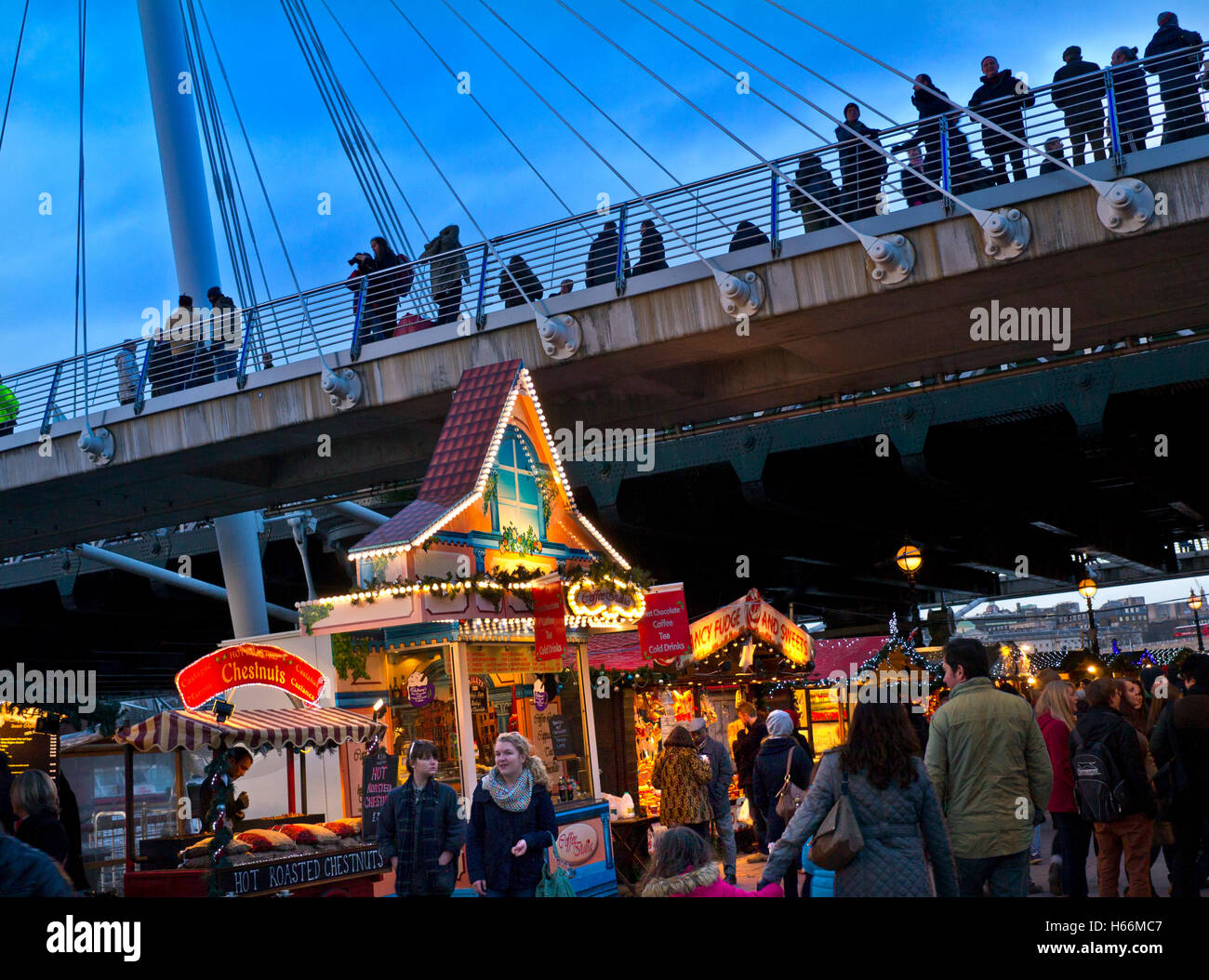 South Bank Christmas market stalls and shoppers with Jubilee Bridge behind at dusk London UK