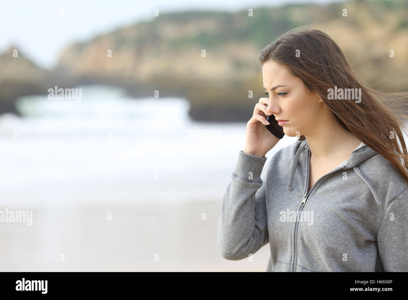 Sad teen talking on the phone on the beach Stock Photo