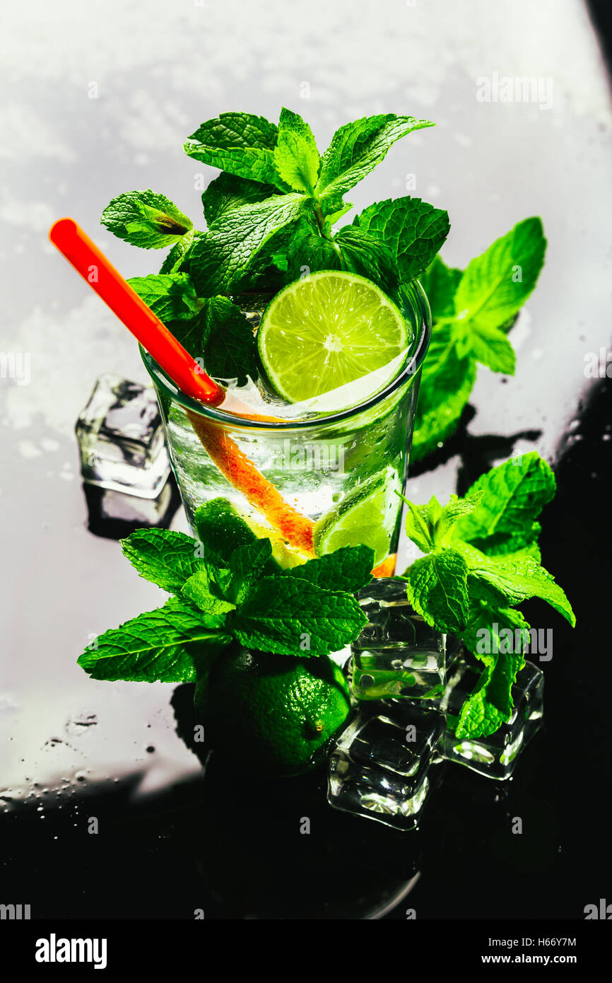 glass of mojito with lime and mint ice cube closeup with red straw