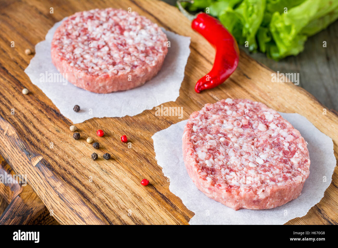 Raw fresh burger meat patties on wooden chopping board. Close up Stock Photo