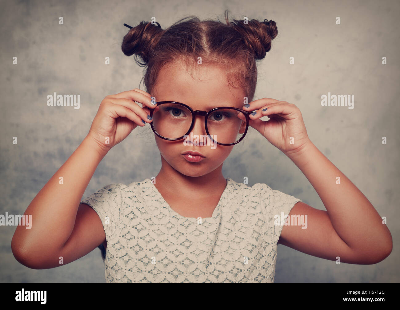 Serious angry kid girl with modern hair style in fashion glasses looking and holding the eyeglasses with empty copy space backgr Stock Photo