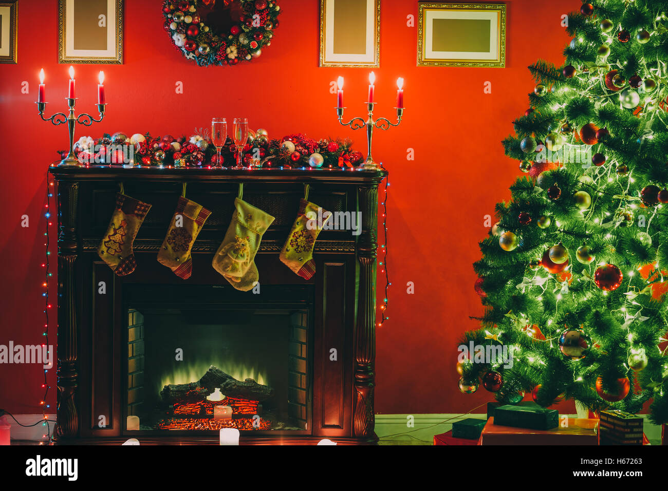 Beautiful decorated Christmas tree with red and goldish baubles and garland, in the new-year background with fireplace and socks Stock Photo