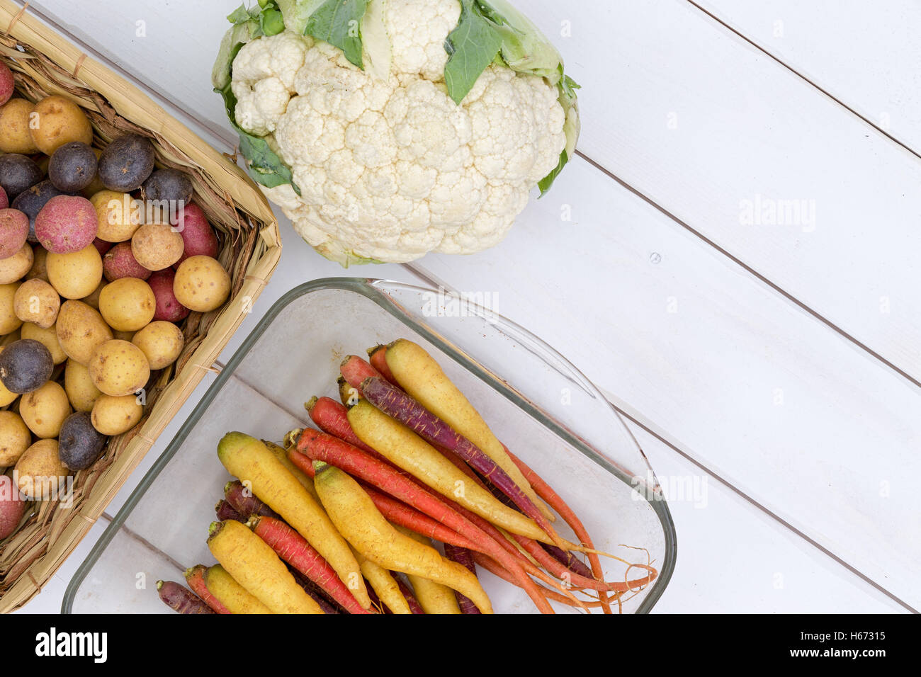Raw cauliflower head beside purple, red and yellow carrots and potatoes over white wooden background Stock Photo