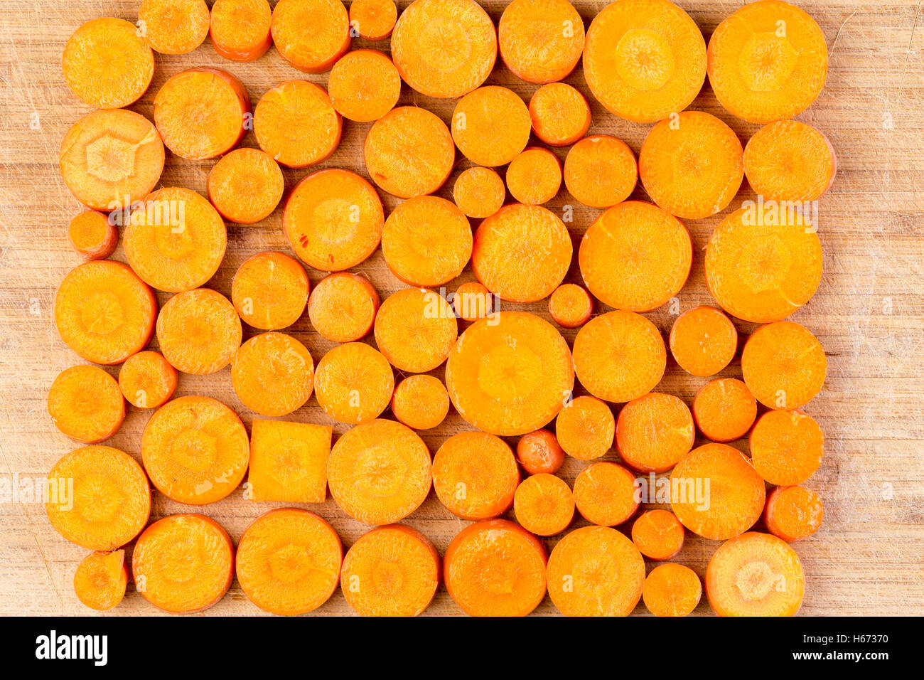 Top down view on chopped circular and rectangular orange colored carrots arranged in neat rows on cutting board Stock Photo
