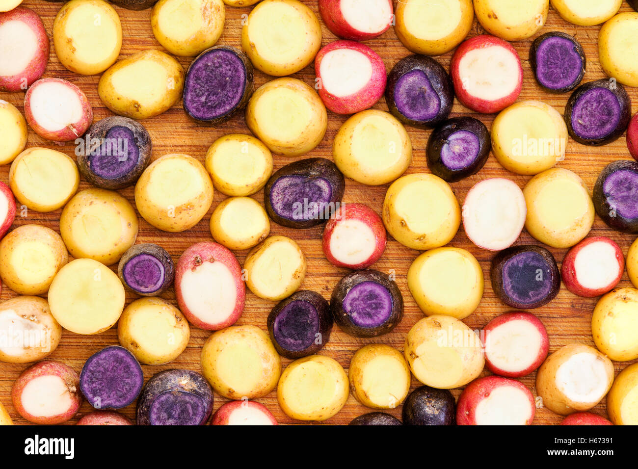 Full frame potato slice background in red, yellow and purple varieties on cutting board for concept about getting ready to roast Stock Photo