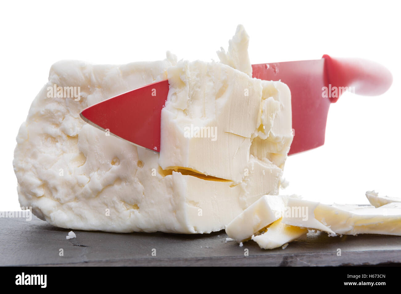 Red ceramic knife slicing through full cream feta cheese made with cow milk in a close up view of the crumbly creamy texture Stock Photo