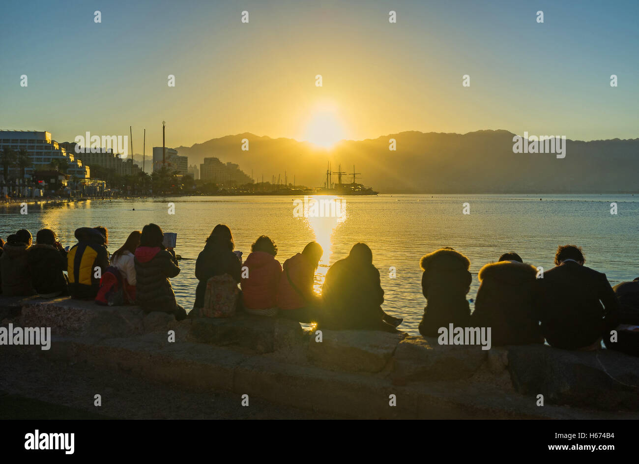 The beautiful sunrise over the North beach with the group of religious tourists, reading the Bible on the shore, Eilat, Israel. Stock Photo