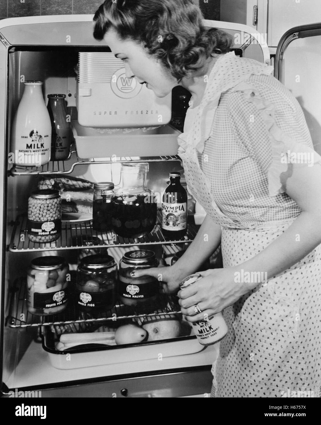 Woman at Refrigerator filled with Food Products in Glass Jars due to Restriction of Metal Products because of Military Needs during World War II, USA, by Office of War Information, January 1943 Stock Photo