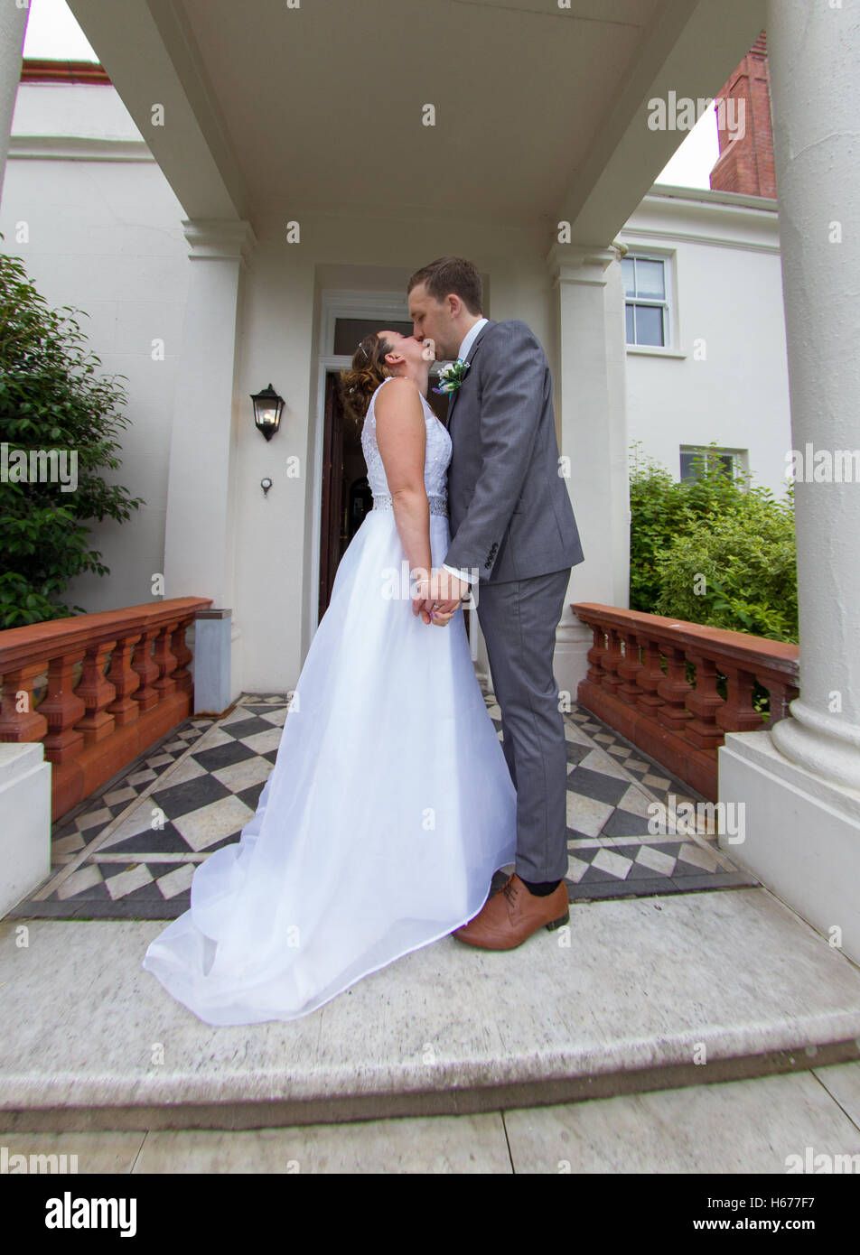 Bride and groom kissing on the steps of their wedding venue. Full length shot of the newly wed husband and wife Stock Photo