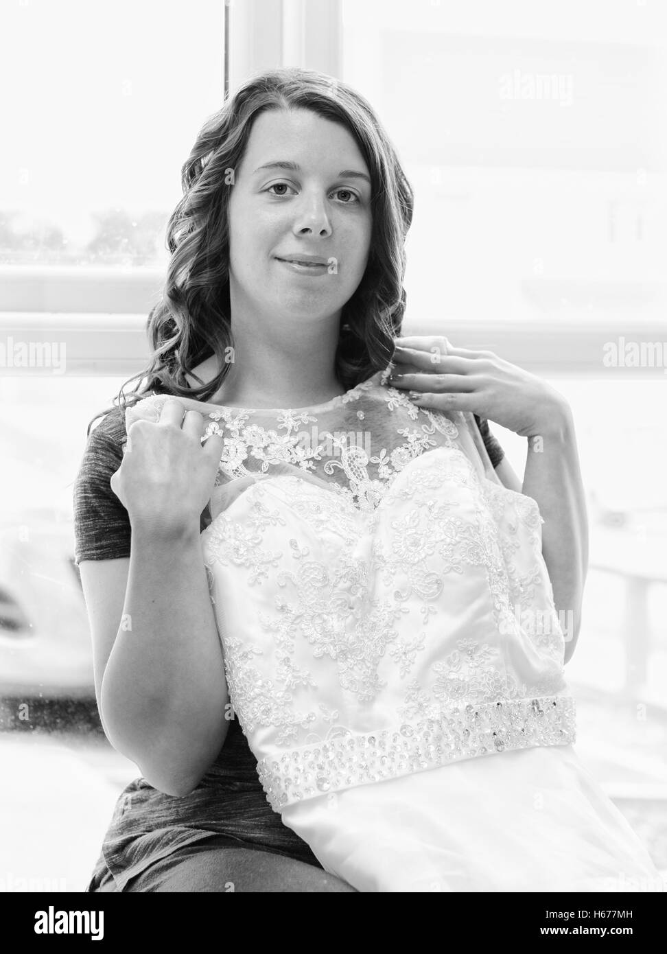 Excited bride to be holding up her wedding dress, taken in vertical format in black and white Stock Photo