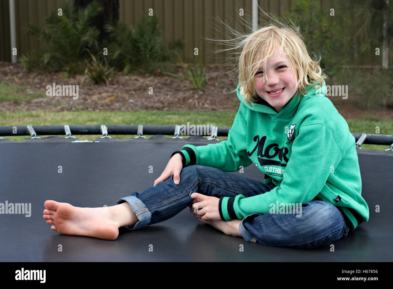 Blonde haired boy sitting smiling on trampoline. Stock Photo