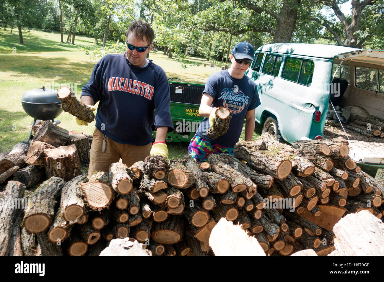 Father and son stacking firewood cut from downed tree. Transported with