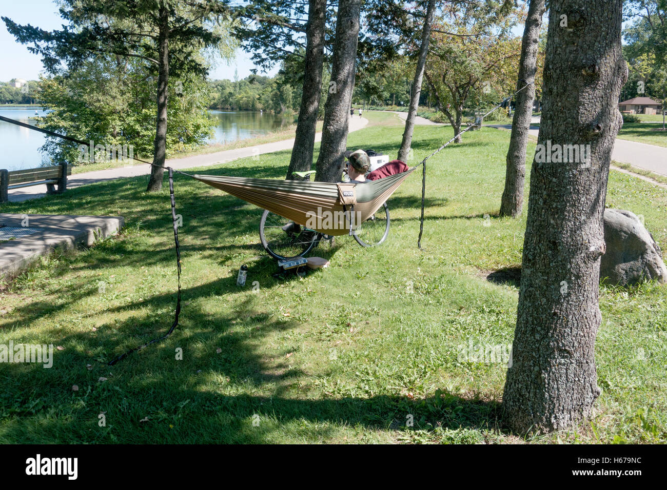 Bicycler relaxing in a hammock enjoying the vista of Lake Calhoun & probably reading a good novel. Minneapolis Minnesota MN USA Stock Photo