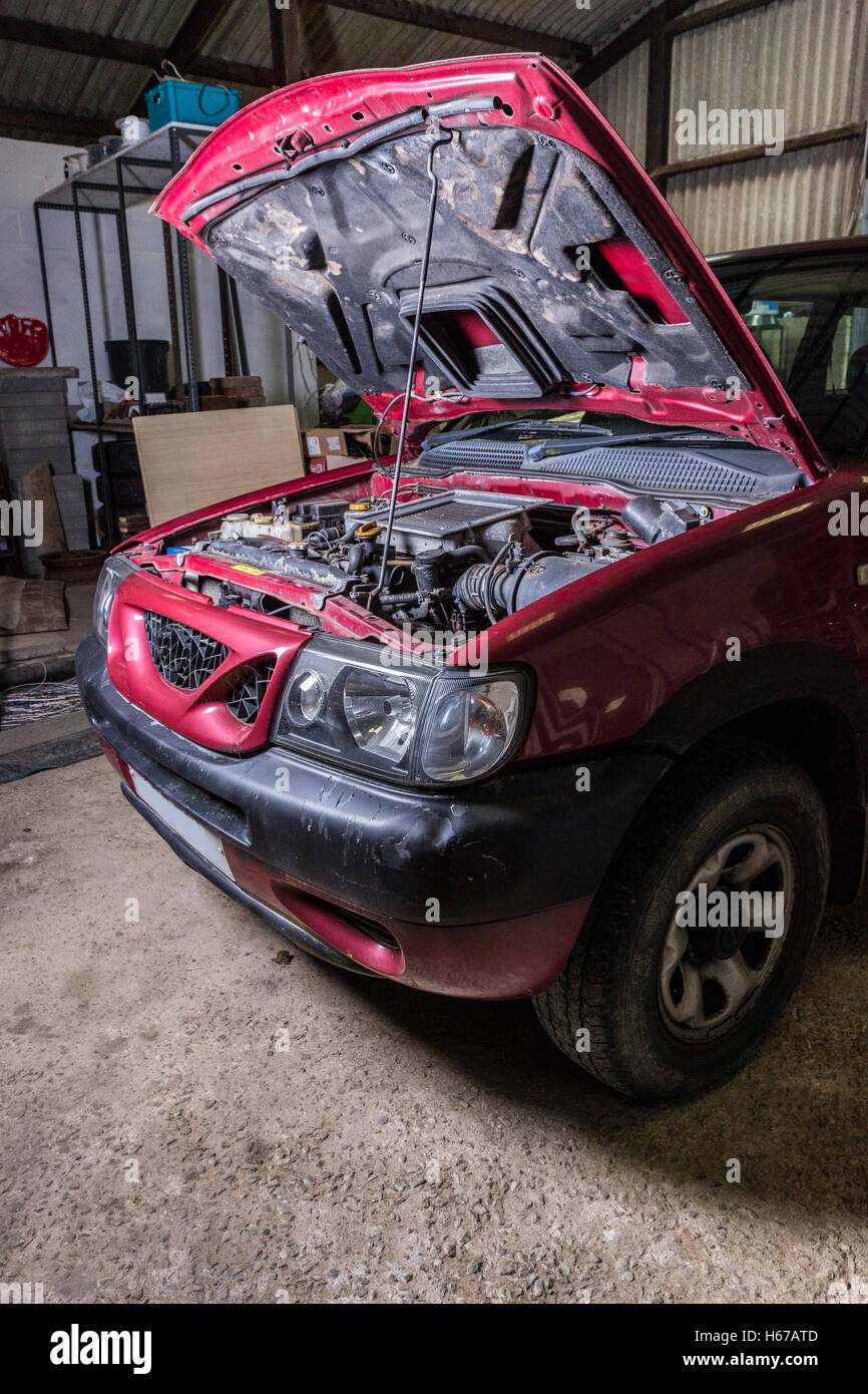 Vertical shot of car in garage with bonnet up being repaired or serviced. Stock Photo