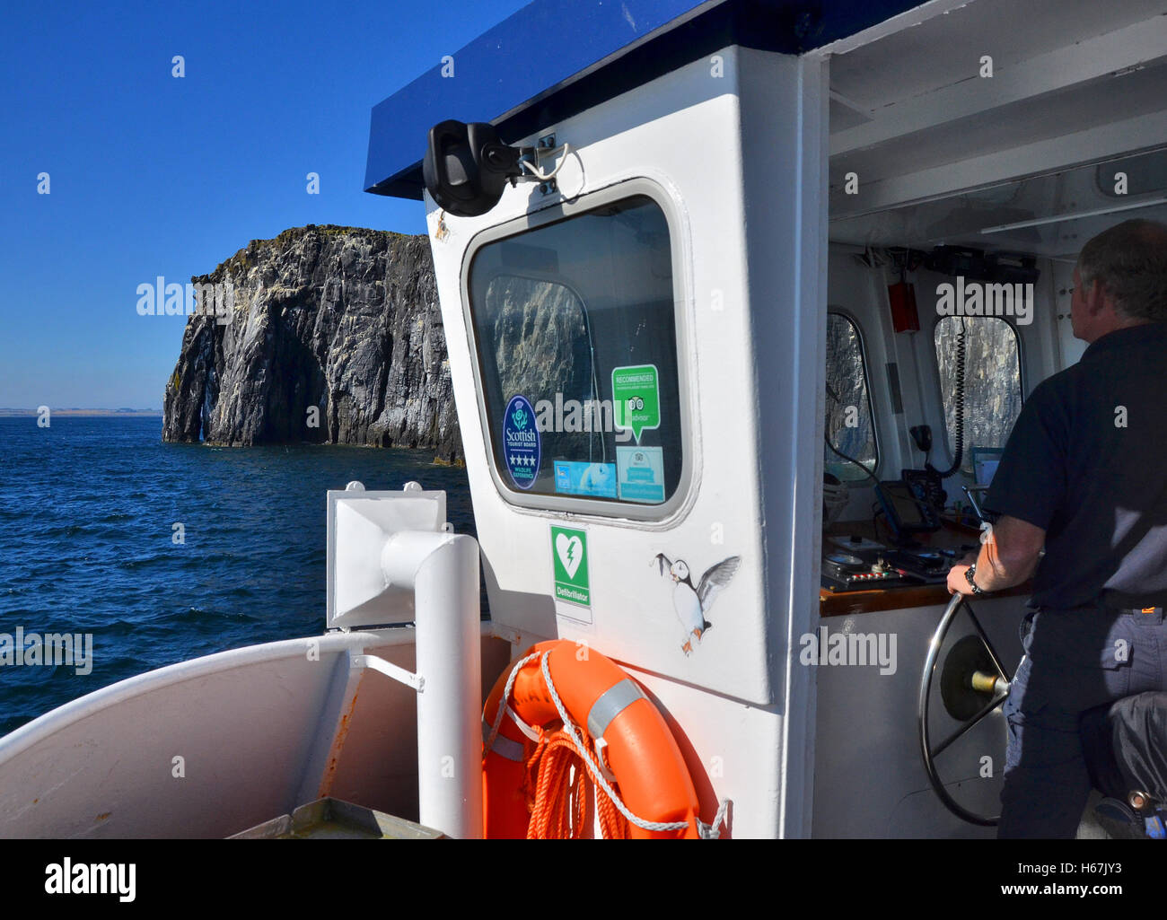 Isle of May, Fife,  as seen from the front of a day trip cruise boat with the captain / skipper at the wheel, steering the boat. Stock Photo