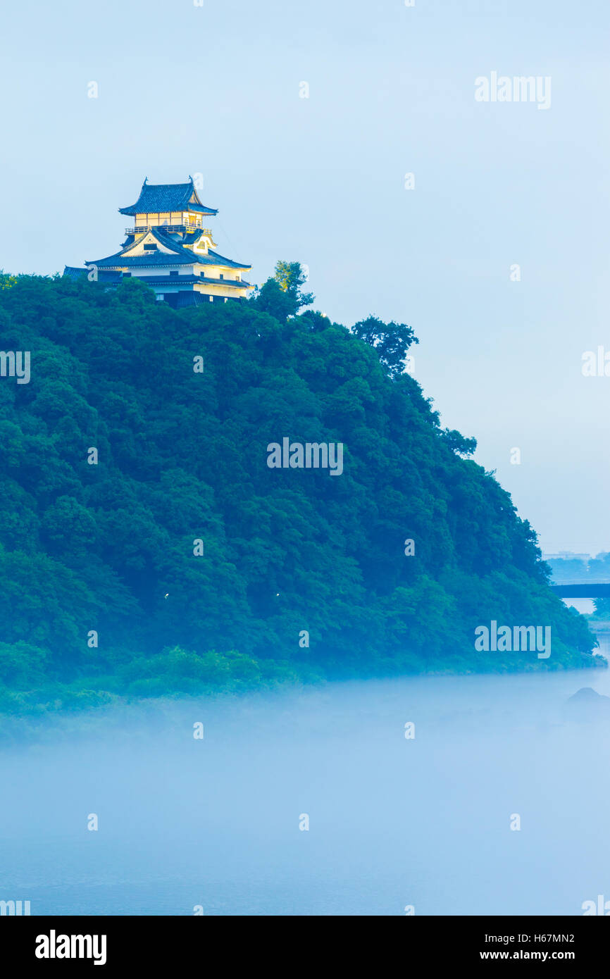 A beautiful layer of mist covers the Kiso River below a lighted Inuyama Castle at evening in Gifu Prefecture, Japan. Vertical Stock Photo