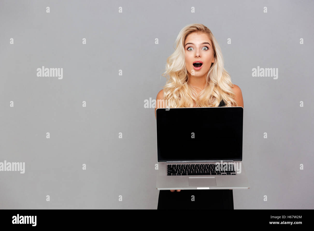 Portrait of a happy excited woman pointing finger on blank laptop computer screen isolated on a white background Stock Photo